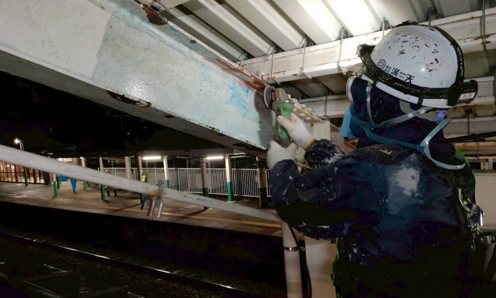 新潟県内の駅ホームで鉄骨梁のサビと旧塗膜を削り落とす3種ケレン作業(素地調整)を行う塗装職人の様子